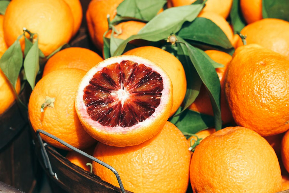 Ein Korb mit Orangen, eine aufgeschnittene Blutorange zeigt das dunkelrote Fruchtfleisch